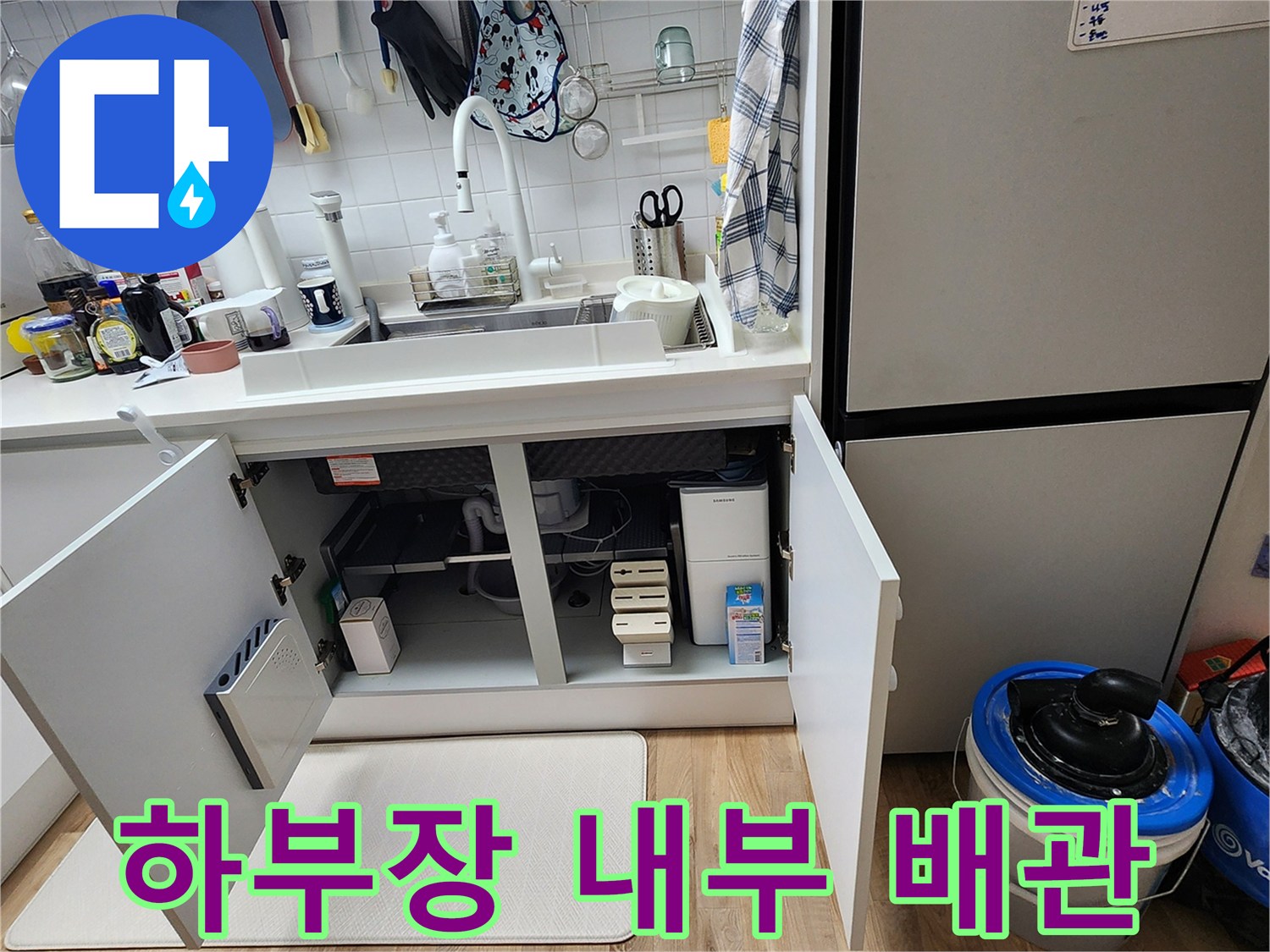 싱크대 하부장 내부의 분배기와 배관 연결 부위를 촬영한 사진입니다.