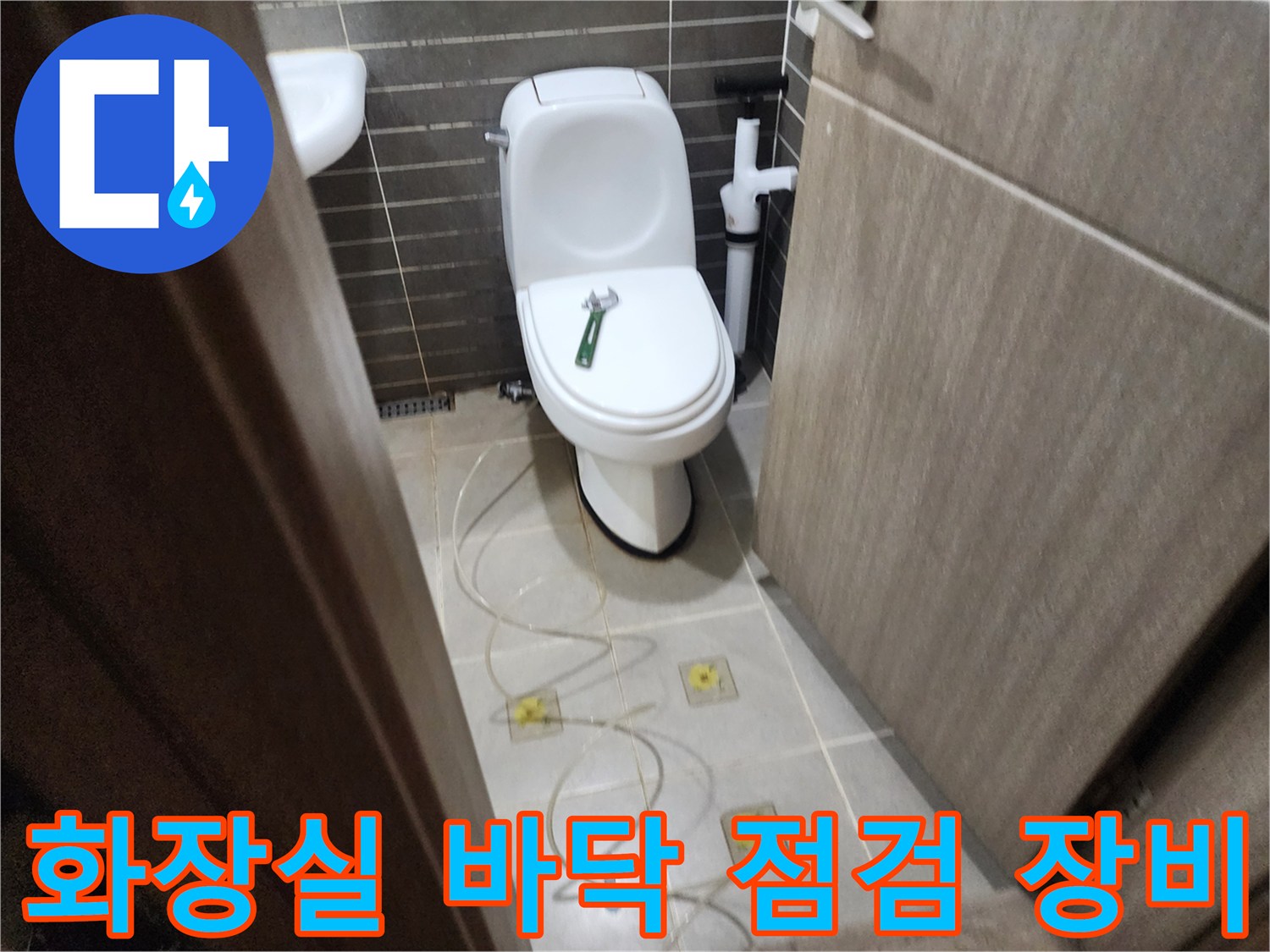 변기 옆 타일에 놓인 점검용 호스와 배관 부위입니다.