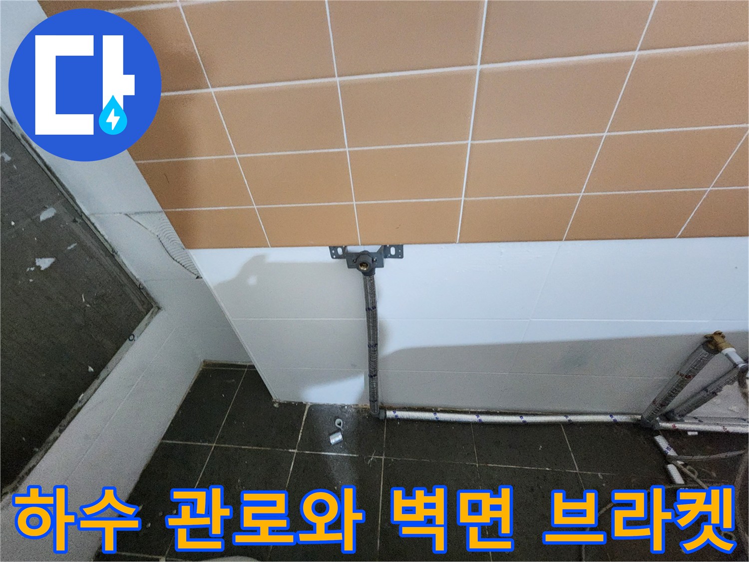 벽면 타일 아래 설치된 하수 배관과 고정용 브라켓 상세 사진