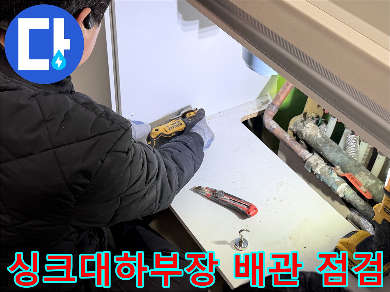 싱크대 하부장 내부의 노후된 배관과 작업 도구 모습