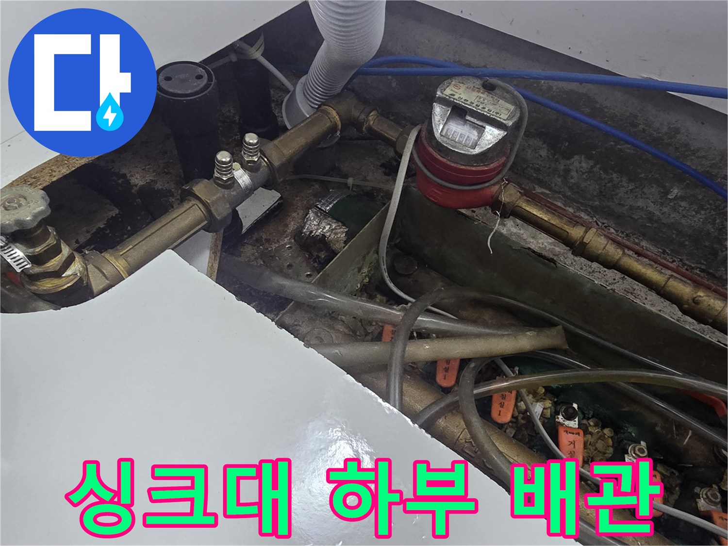복잡하게 연결된 싱크대 하부의 급수 배관과 계량기 사진입니다.