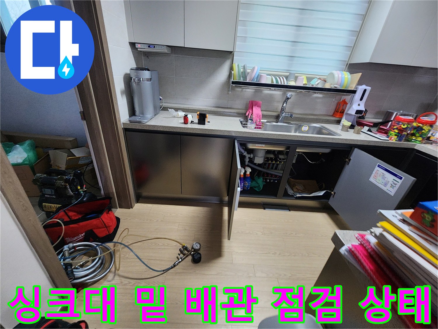 열려있는 싱크대 하부장-복잡한 분배기 배관과 작업용 장비가 놓인 모습