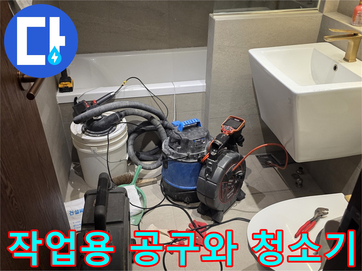 세면대 옆 바닥에 놓인 습식 청소기와 배관 작업용 수공구들