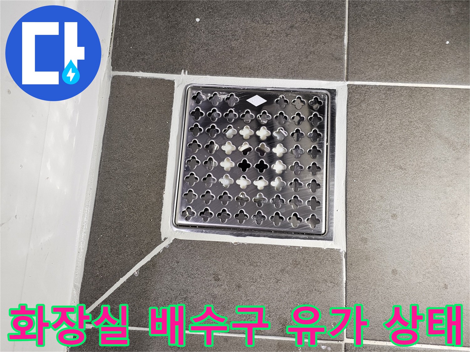 어두운색 타일과 은색 배수구 거름망이 설치된 화장실 바닥 모습
