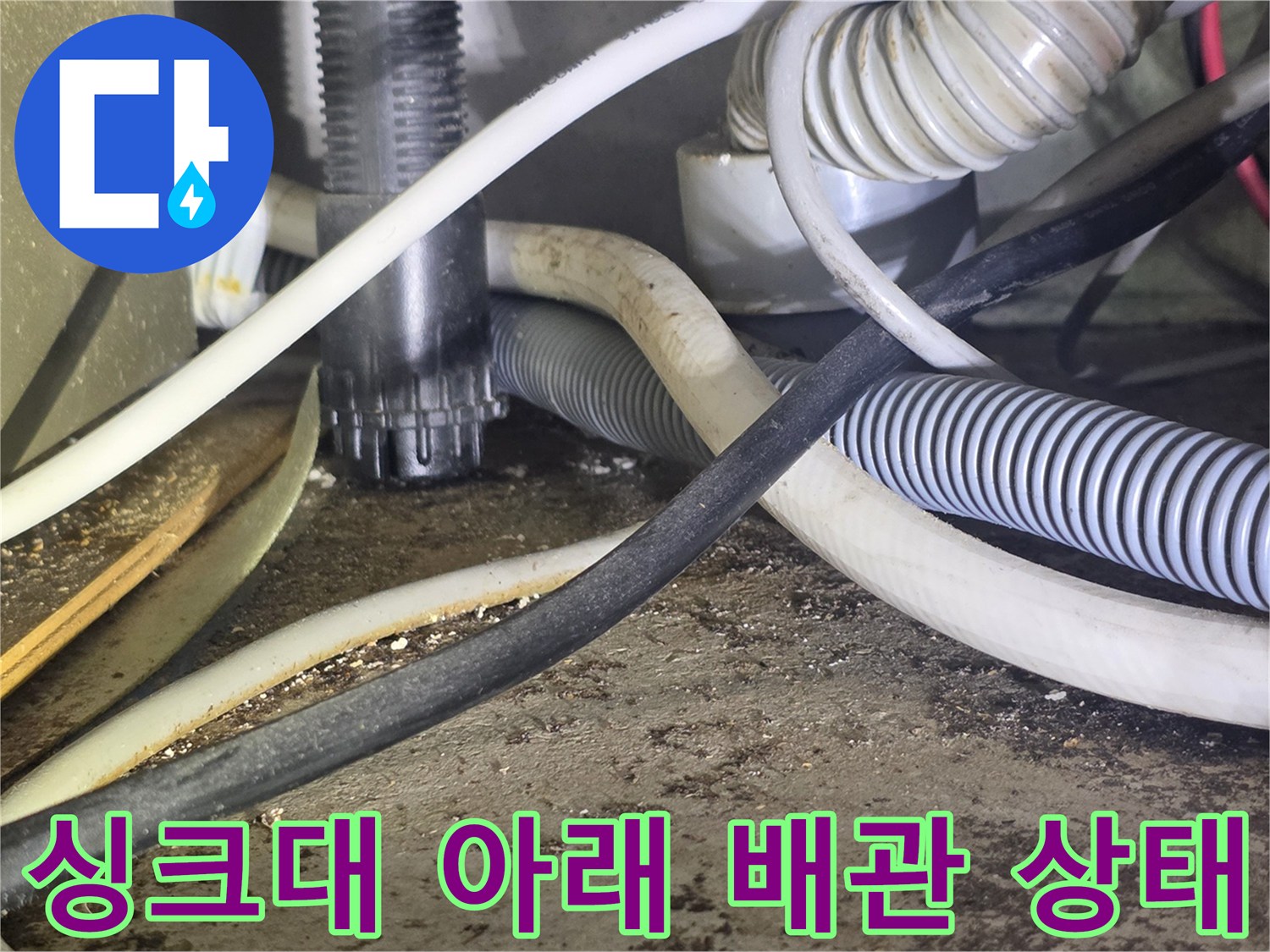 싱크대 하부장 내부의 굵은 하수 배관과 유연한 호스들이 복잡하게 연결된 모습입니다.
