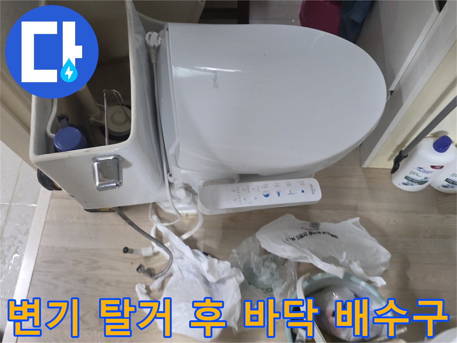 변기 하부의 노출된 배관과 작업용 세제 용기들