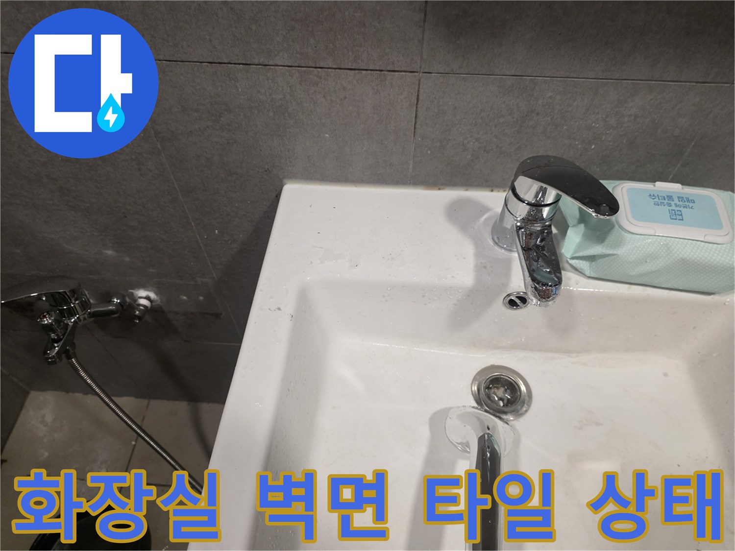 세면대 뒤편의 회색 타일과 수전 설치 모습