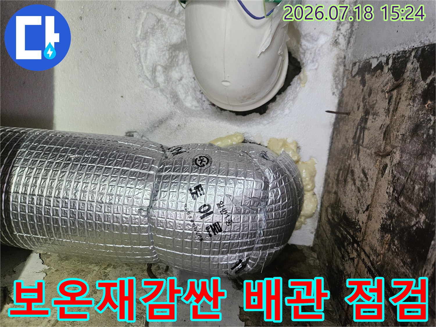 은색 보온재로 감싸진 수직 배관과 상부 고정 장치 모습