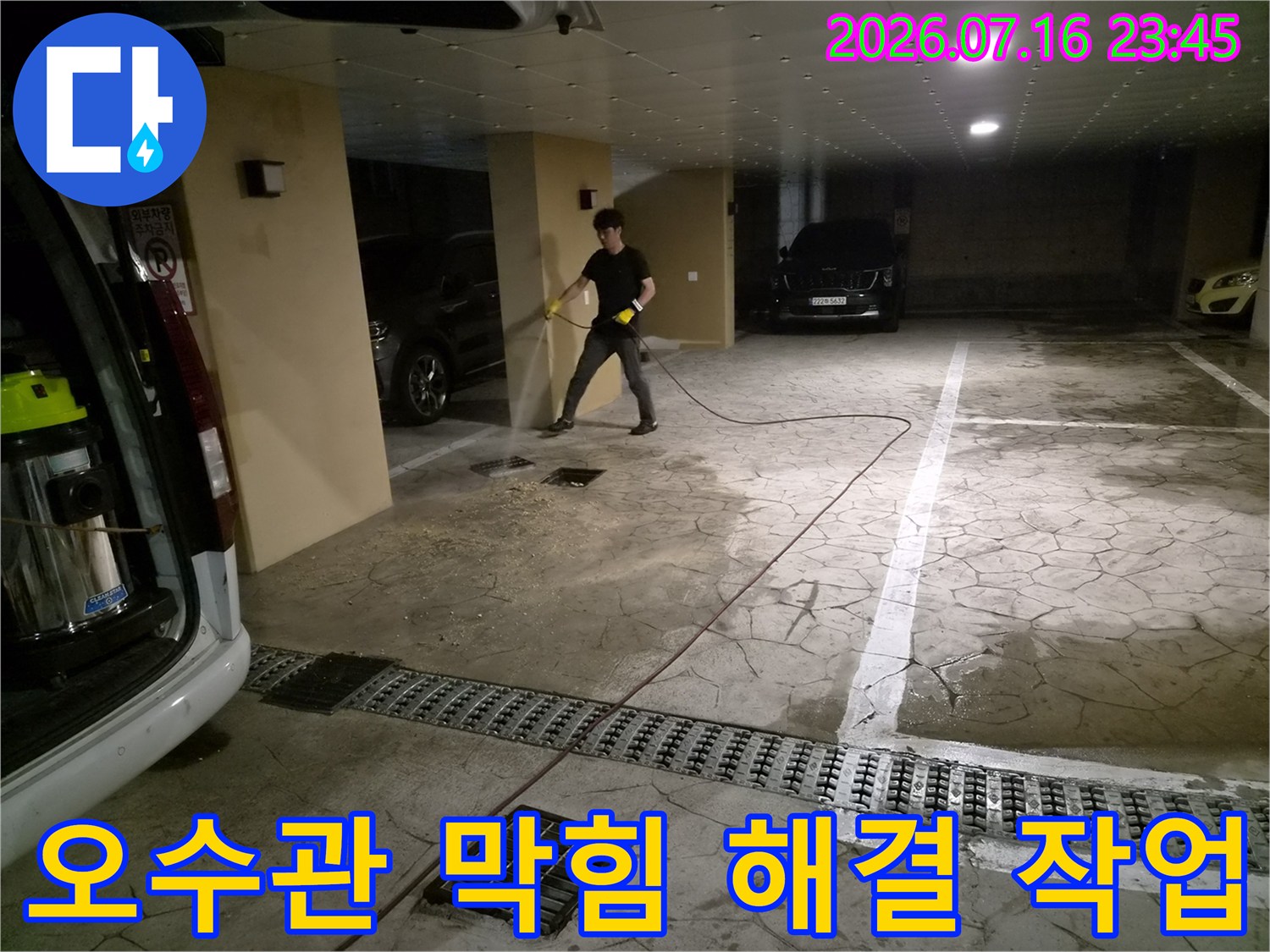 고압 세척기를 사용하여 주차장 배수구의 이물질을 밀어내는 현장 사진