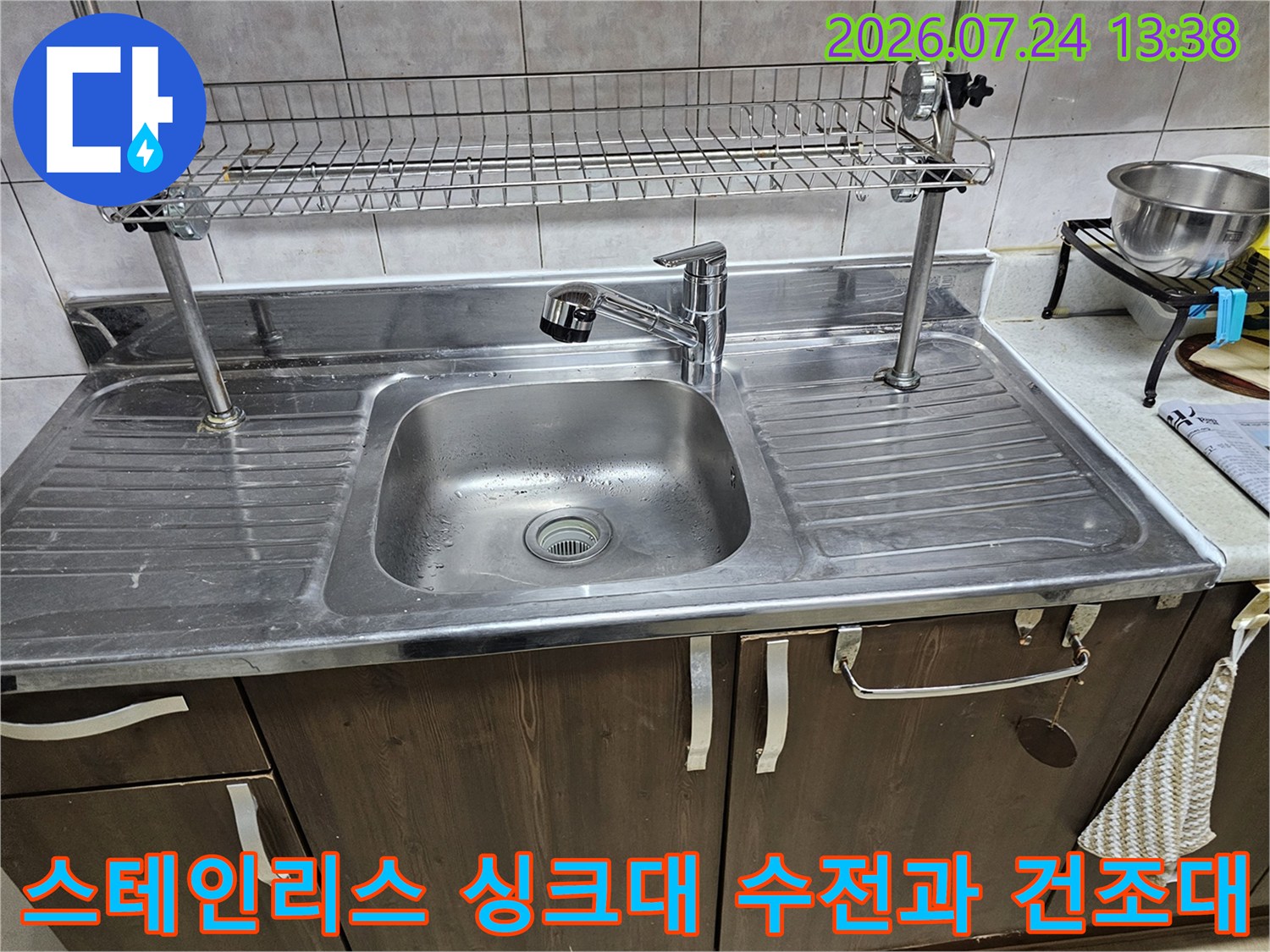 주방의 스테인리스 싱크볼-상단에 고정된 금속제 선반과 수전 모습