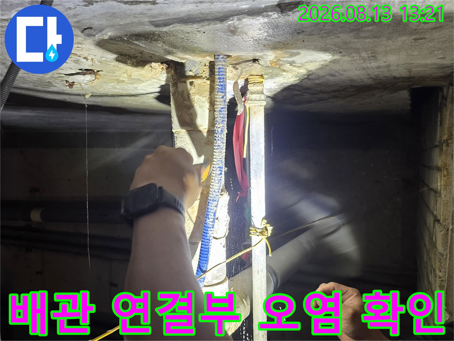 손전등을 사용하여 배관 꺾임 구간의 습기와 오염 상태를 상세히 관찰하는 장면입니다.