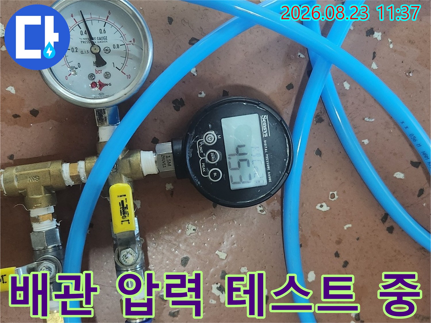 파란색 호스로 연결된 배관의 디지털 압력 게이지 화면입니다.