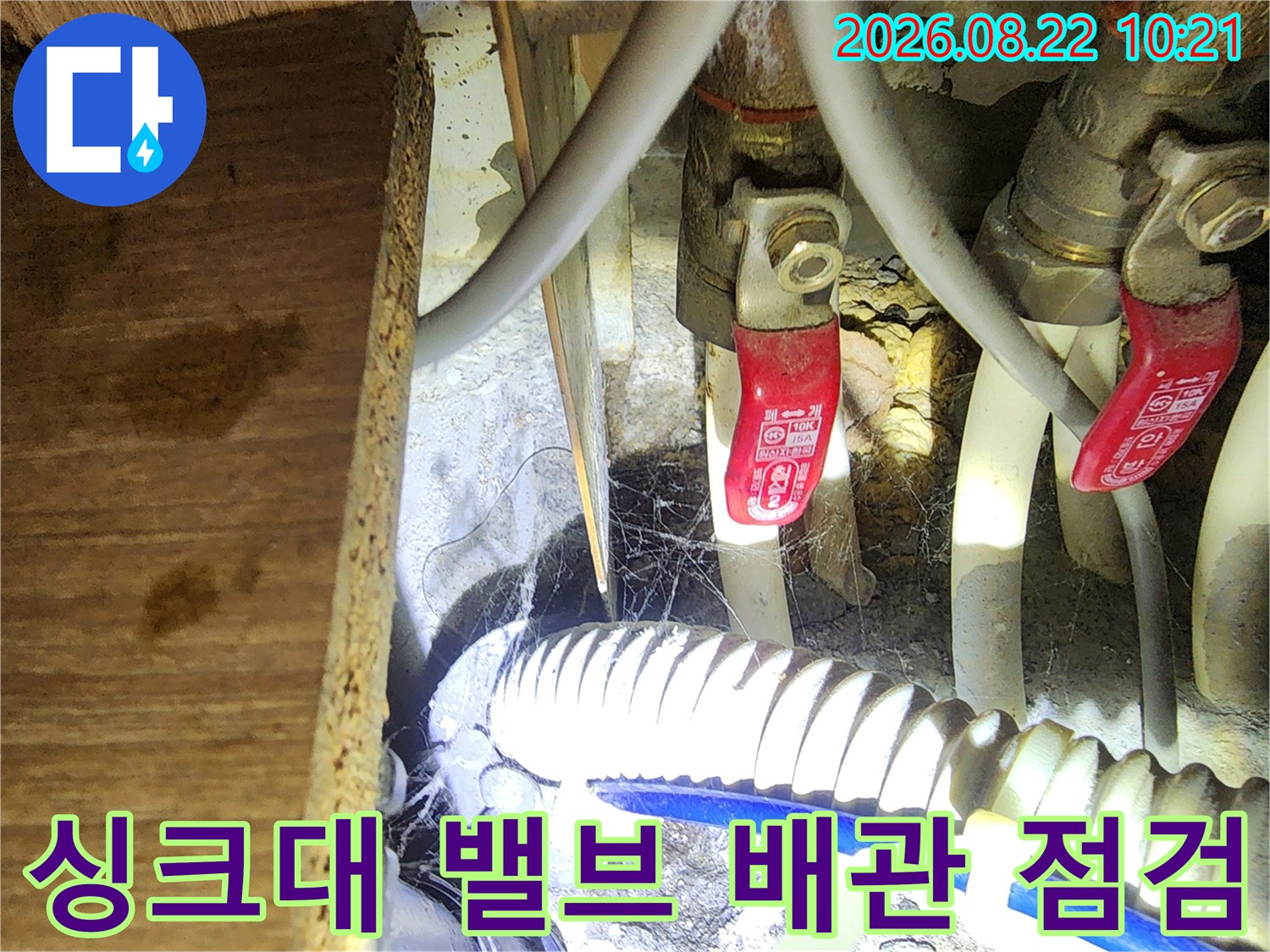 싱크대 하부의 빨간색 밸브와 흰색 배수 호스 모습