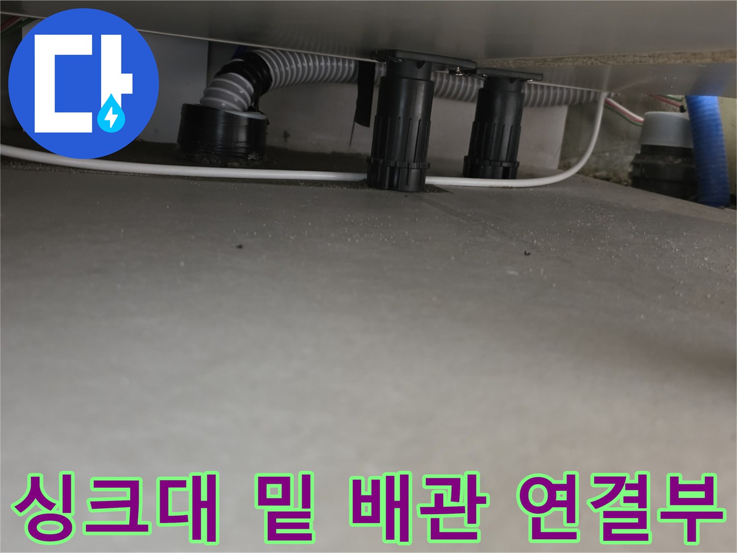 싱크대 아래쪽의 회색 주름관과 검은색 플라스틱 부속품들