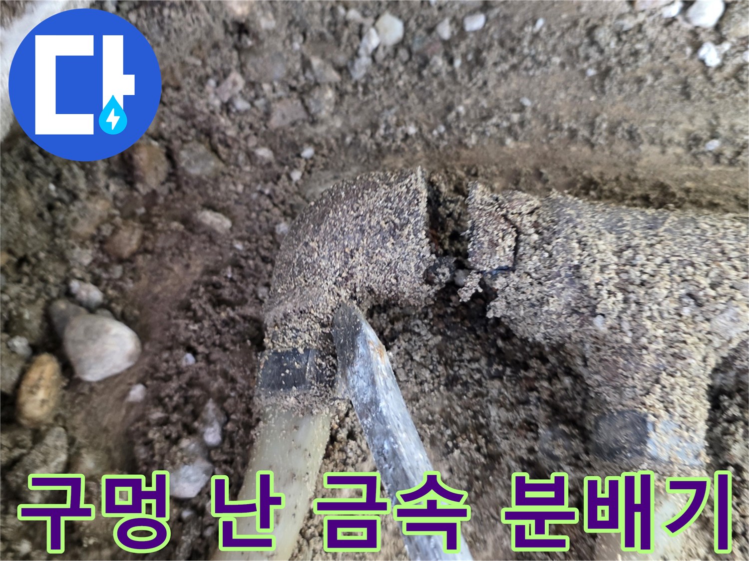 자갈과 흙 사이로 노출된 부식된 배관 조각