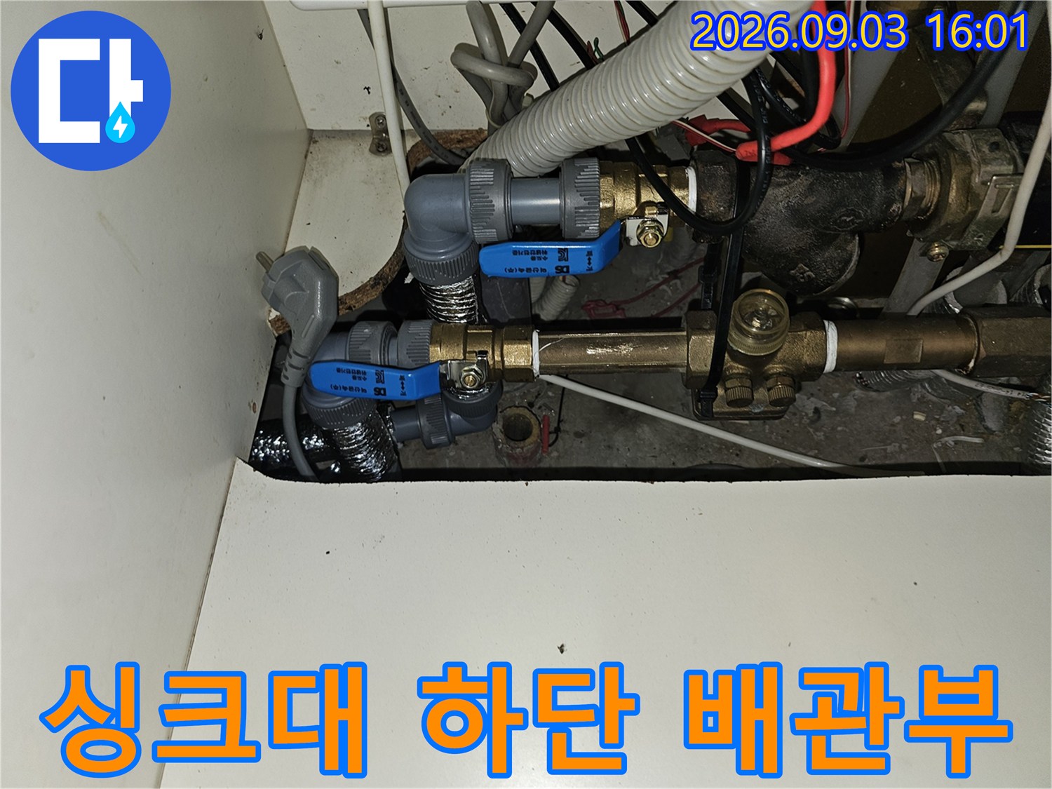 파란색 밸브와 금속 부품이 연결된 싱크대 하부 배관 모습입니다.