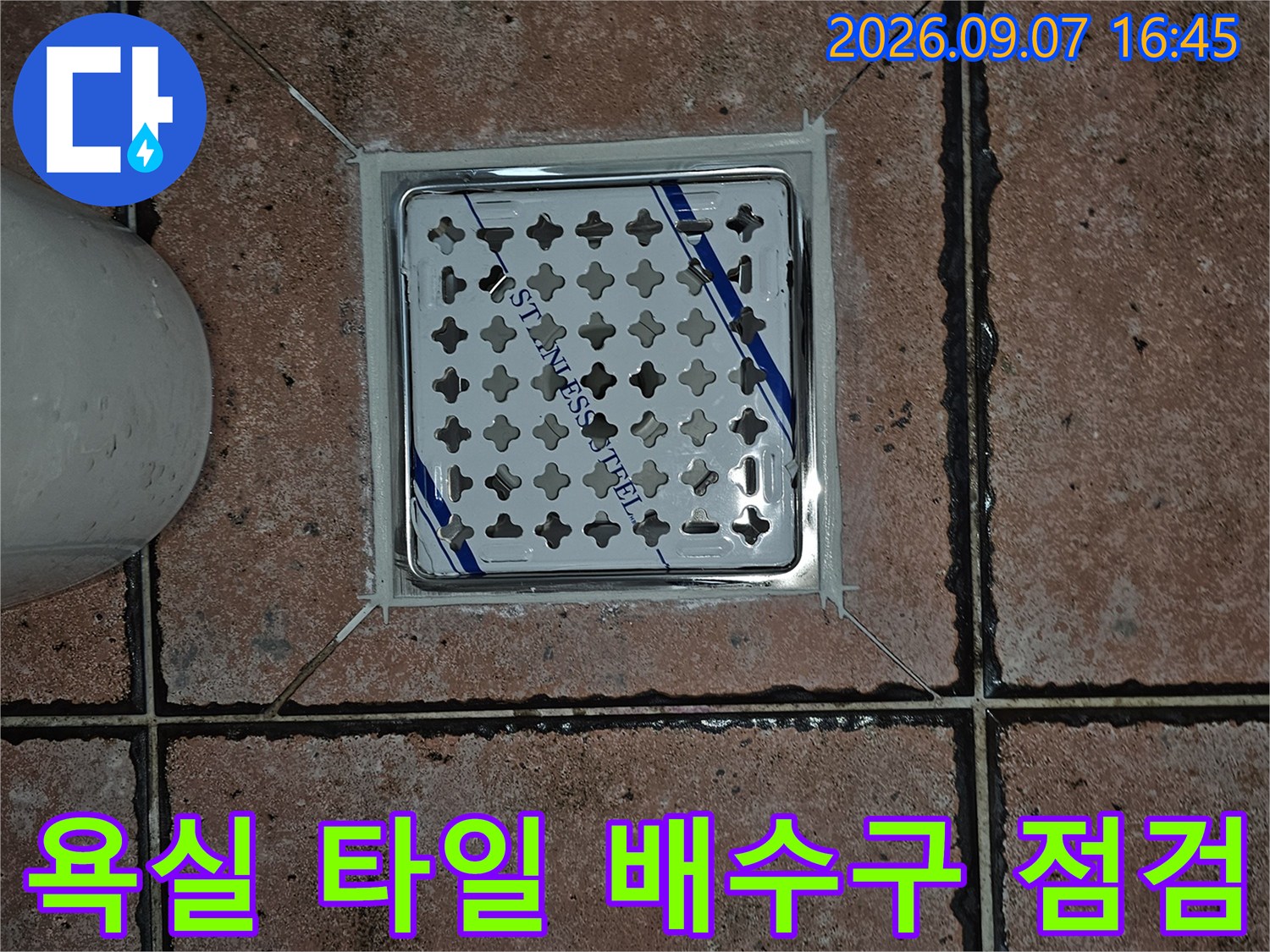 스테인리스 재질의 배수구 유가와 주변 타일 줄눈을 근접 촬영한 사진입니다.