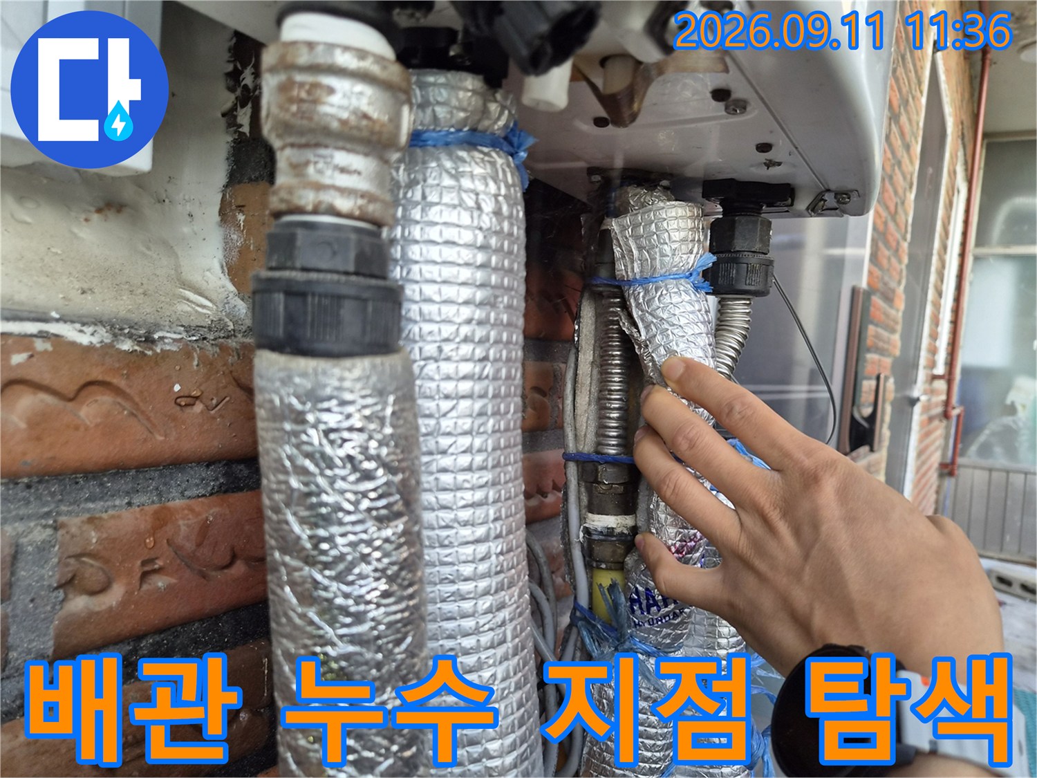 손으로 보일러 하단 배관의 상태를 확인하며 점검하는 장면입니다.